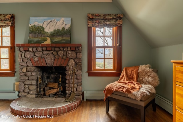 sitting room with a baseboard radiator, lofted ceiling, and a stone fireplace