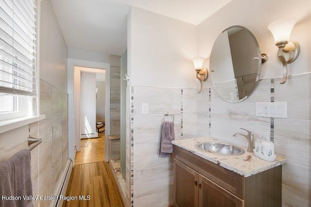 bathroom featuring vanity, wood-type flooring, tile walls, and a baseboard heating unit