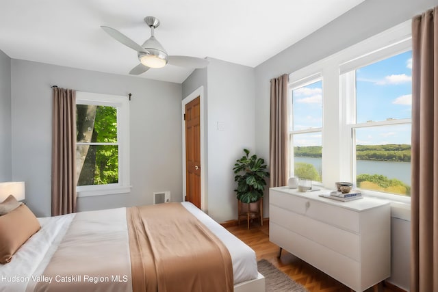 bedroom with hardwood / wood-style flooring, ceiling fan, a water view, and multiple windows