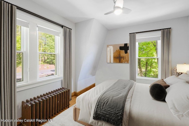 bedroom featuring hardwood / wood-style floors, radiator heating unit, multiple windows, and ceiling fan