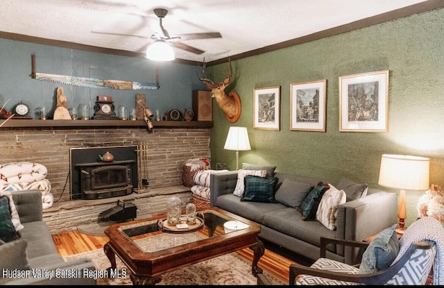 living room featuring ceiling fan, wood-type flooring, a wood stove, and crown molding