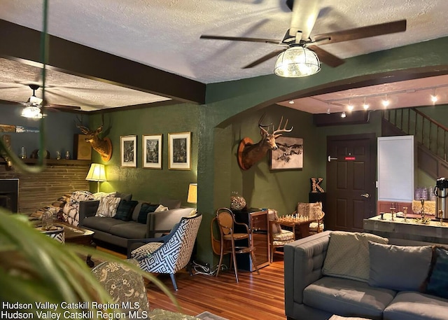 living room with hardwood / wood-style flooring, ceiling fan, beam ceiling, and a textured ceiling