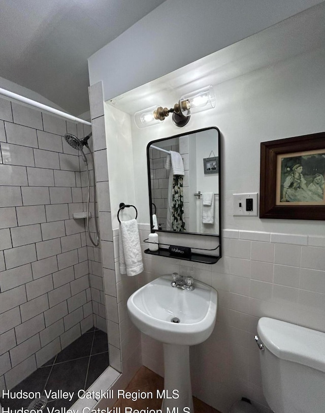 bathroom featuring tile patterned flooring, toilet, a tile shower, and tile walls