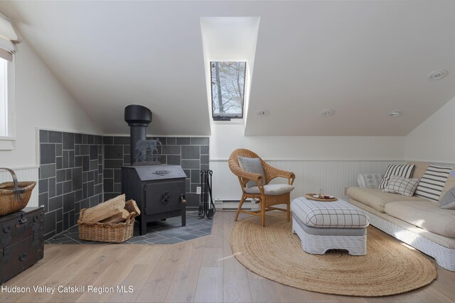 196 Wellington Ln, Cooperstown, NY 13326 - living room featuring wood finished floors, baseboard heating, lofted ceiling, wainscoting, and a wood stove