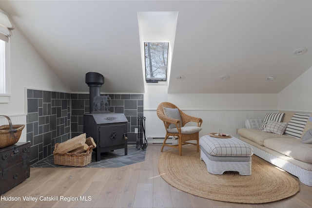 196 Wellington Ln, Cooperstown, NY 13326 - living area featuring wood finished floors, a baseboard heating unit, a wainscoted wall, lofted ceiling, and a wood stove