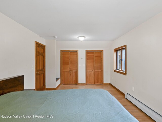 bedroom with two closets, a baseboard radiator, and light hardwood / wood-style flooring