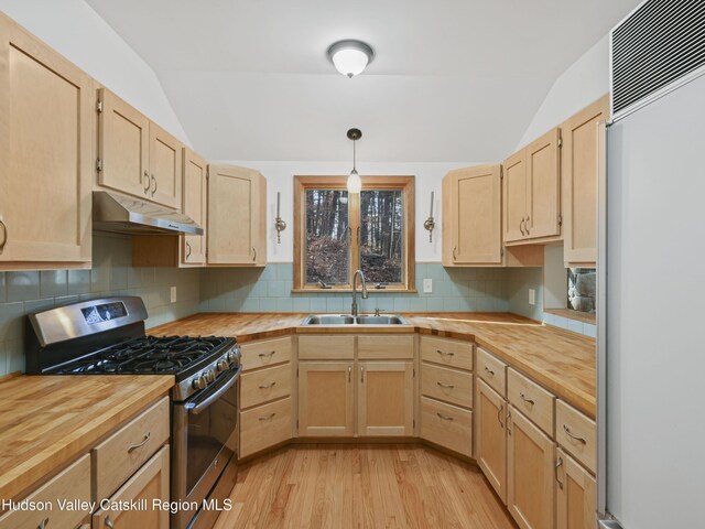 kitchen featuring stainless steel gas stove, sink, paneled fridge, pendant lighting, and vaulted ceiling