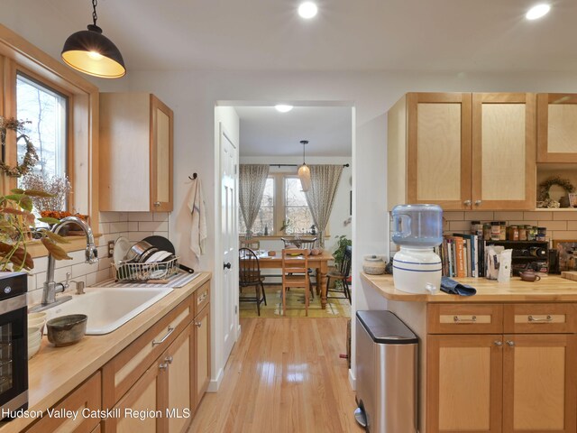 kitchen with tasteful backsplash, sink, pendant lighting, light brown cabinets, and light hardwood / wood-style floors