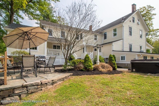 rear view of house featuring a lawn, a patio, and a hot tub