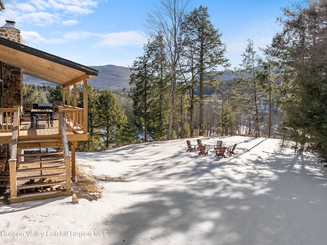 yard layered in snow with a deck with mountain view and a fire pit