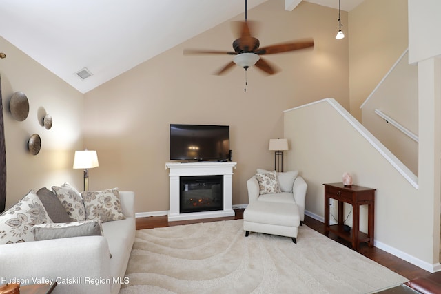 living area with a glass covered fireplace, a ceiling fan, visible vents, wood finished floors, and baseboards
