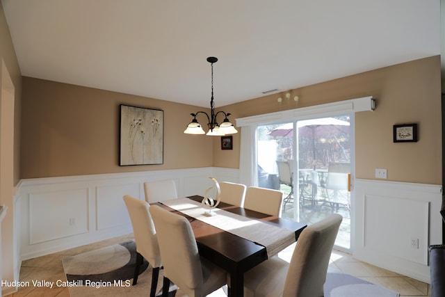 dining room featuring visible vents, light tile patterned floors, a decorative wall, a chandelier, and wainscoting