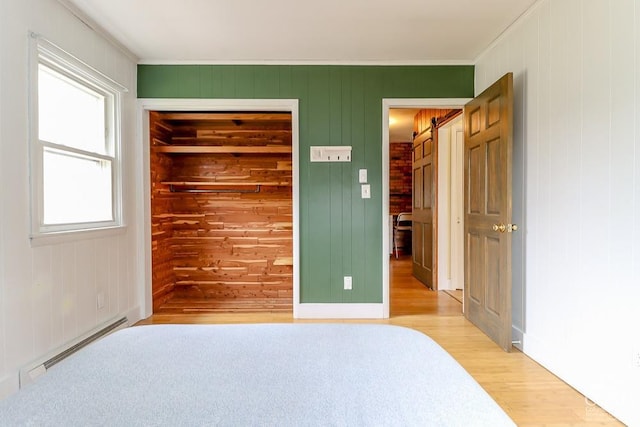 32 Harvey Mountain Rd, Austerlitz, NY 12017 - unfurnished bedroom with a baseboard heating unit, light wood-style floors, ornamental molding, a closet, and wood walls