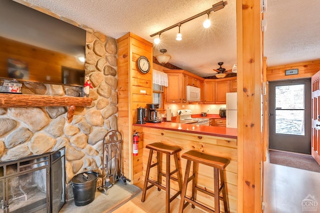 kitchen with white appliances, a textured ceiling, ceiling fan, a fireplace, and a breakfast bar area