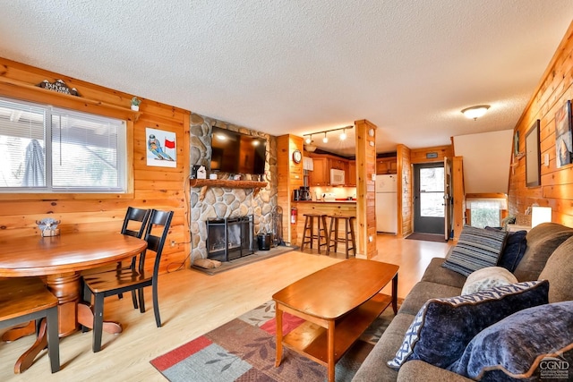living room with a textured ceiling, a stone fireplace, wood walls, light wood-style flooring, and rail lighting