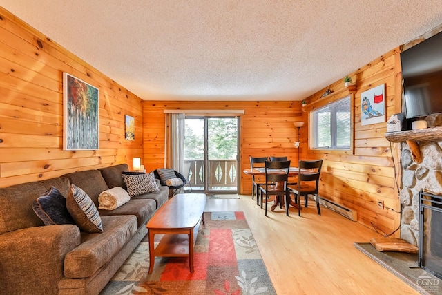 living area with plenty of natural light, a textured ceiling, wood finished floors, wood walls, and a stone fireplace