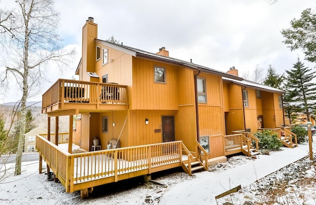 snow covered house with a chimney and a wooden deck