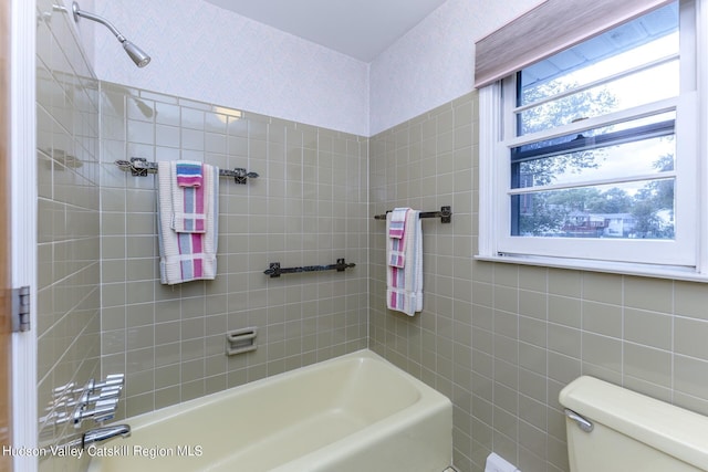 bathroom featuring tiled shower / bath combo, toilet, and tile walls