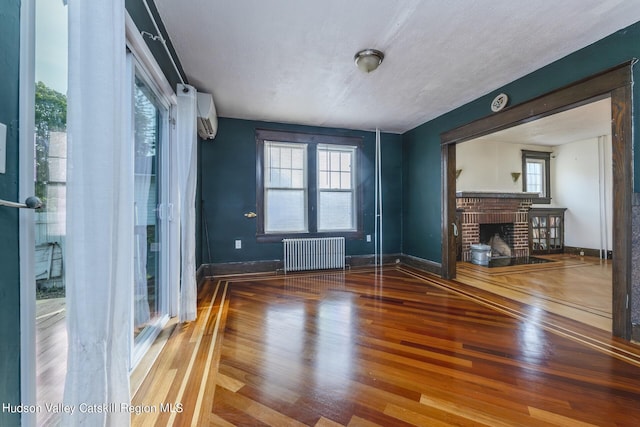 unfurnished living room featuring hardwood / wood-style floors, plenty of natural light, radiator heating unit, and a brick fireplace