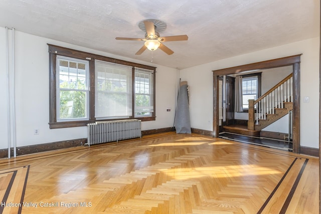 empty room with a wealth of natural light, light parquet floors, radiator, and ceiling fan