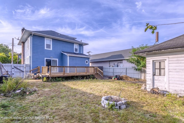 rear view of house with a fire pit, a deck, and a lawn