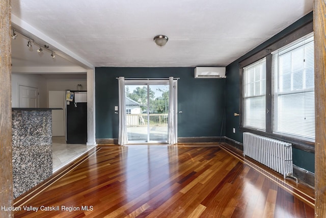 spare room featuring hardwood / wood-style flooring, plenty of natural light, radiator heating unit, and an AC wall unit