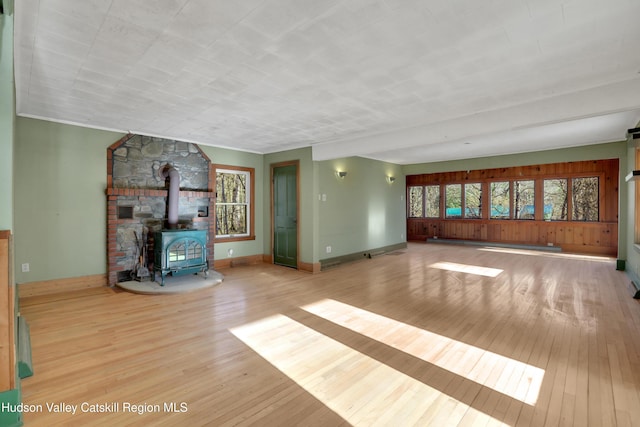 unfurnished living room featuring baseboard heating, a wood stove, a wealth of natural light, and wood-type flooring