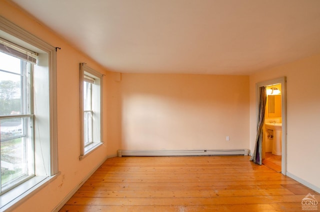 spare room featuring light wood finished floors, a baseboard radiator, and baseboards