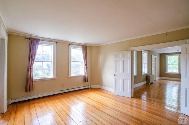 spare room featuring a baseboard heating unit, light wood finished floors, crown molding, and baseboards