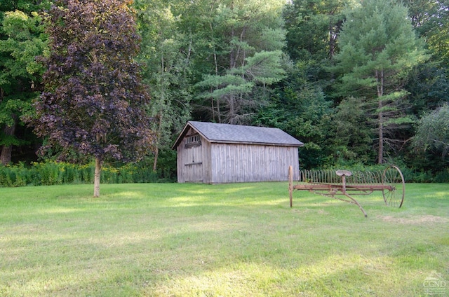 view of grassy yard with an outbuilding, a forest view, and a shed