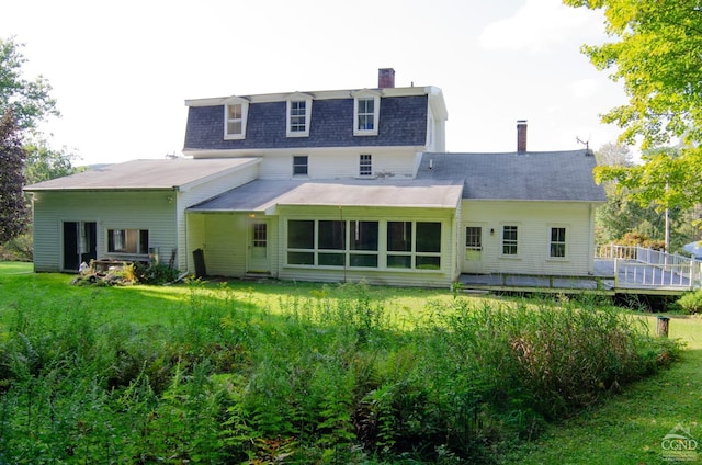 back of property featuring a chimney, a wooden deck, a yard, and mansard roof
