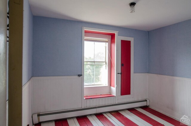 doorway to outside with a baseboard radiator, plenty of natural light, wainscoting, and wood finished floors