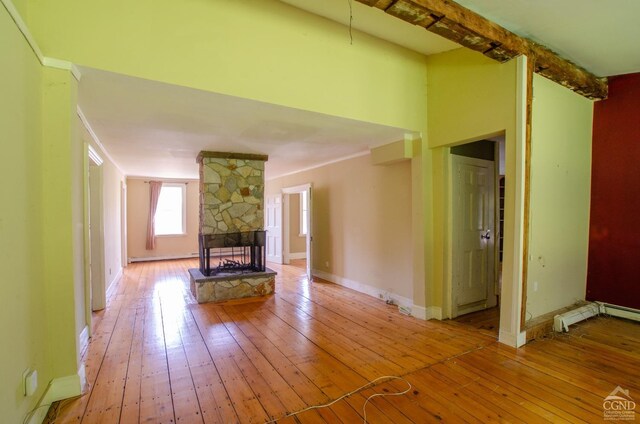 unfurnished living room with hardwood / wood-style flooring, a stone fireplace, beamed ceiling, and baseboards