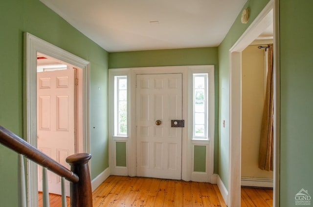 foyer entrance with a baseboard heating unit, light wood-type flooring, and baseboards