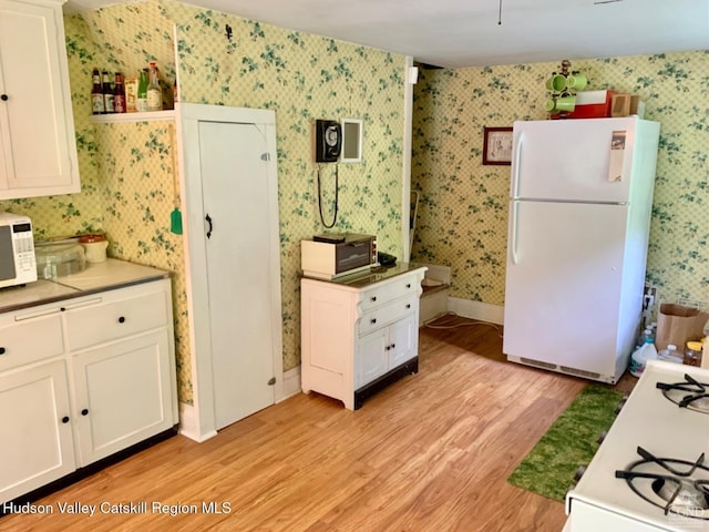 kitchen featuring white appliances, wallpapered walls, light wood finished floors, white cabinetry, and light countertops