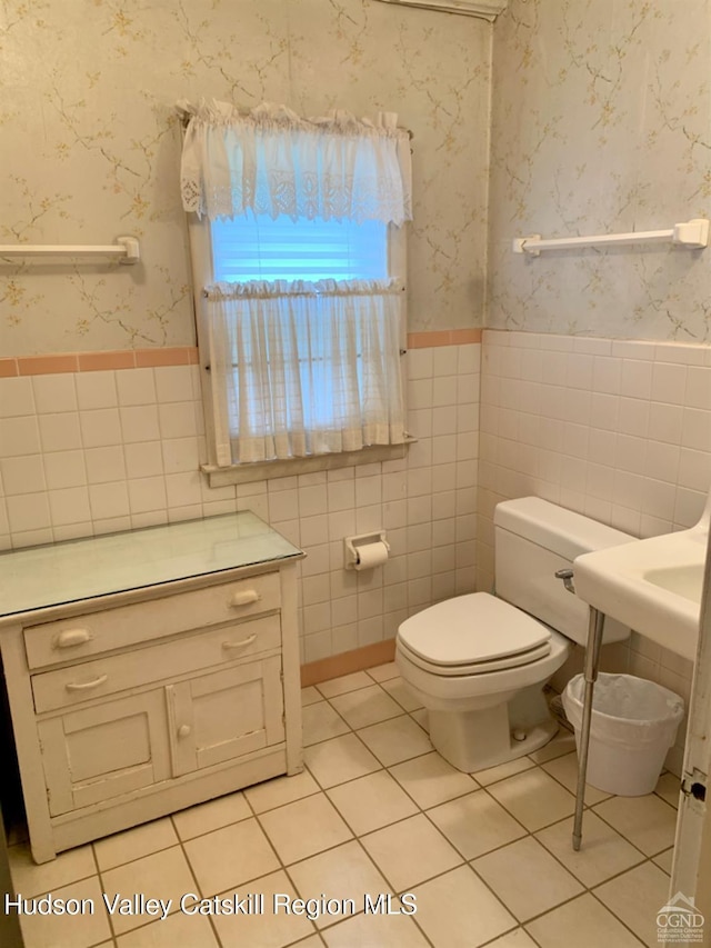 bathroom featuring tile walls, a wainscoted wall, tile patterned flooring, toilet, and wallpapered walls