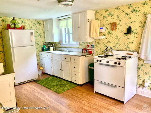 kitchen with wallpapered walls, white appliances, light wood finished floors, white cabinets, and a sink