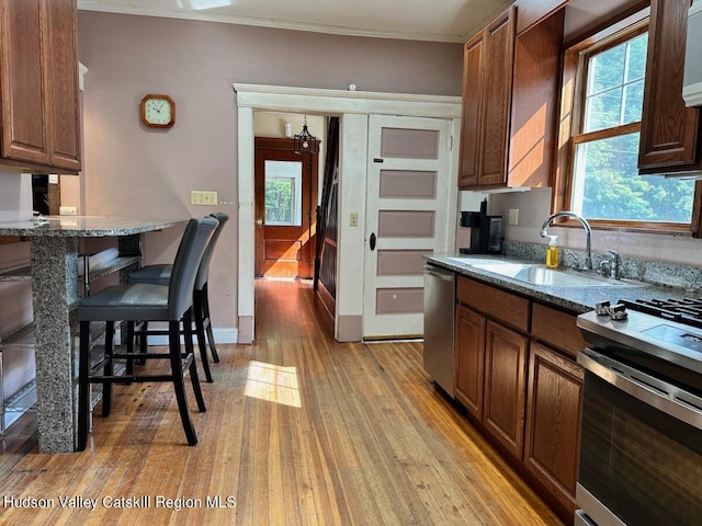 kitchen with stone counters, a breakfast bar area, stainless steel appliances, light wood-style flooring, and a sink