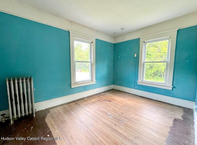 empty room featuring radiator, plenty of natural light, baseboards, and wood finished floors