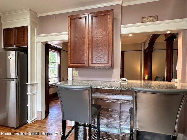 kitchen featuring a peninsula, a kitchen bar, freestanding refrigerator, and brown cabinets