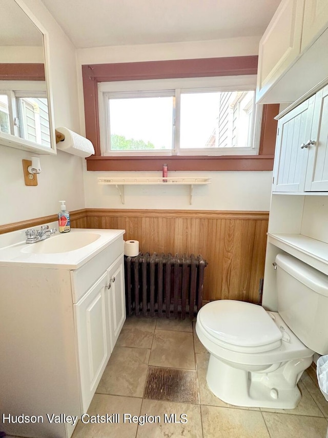 bathroom with toilet, wood walls, vanity, wainscoting, and radiator