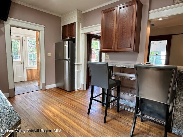 kitchen featuring light wood-style flooring, baseboards, ornamental molding, freestanding refrigerator, and dark stone counters