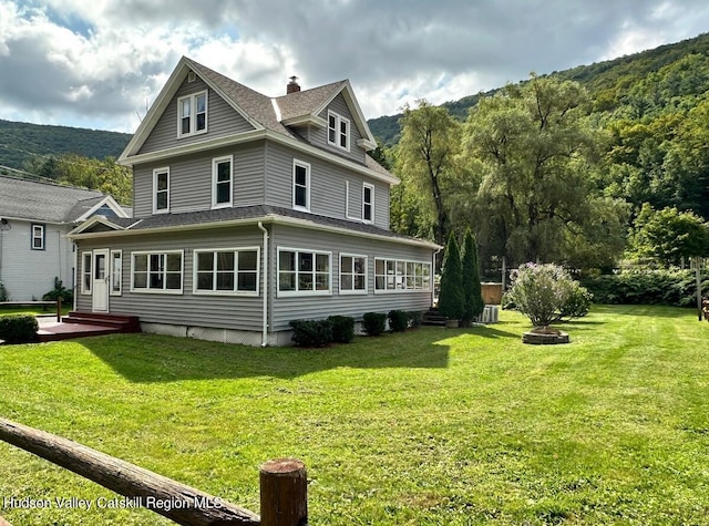 back of property featuring a shingled roof, central air condition unit, a lawn, and a mountain view