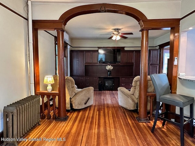 living room featuring radiator heating unit, hardwood / wood-style flooring, ornate columns, and ceiling fan