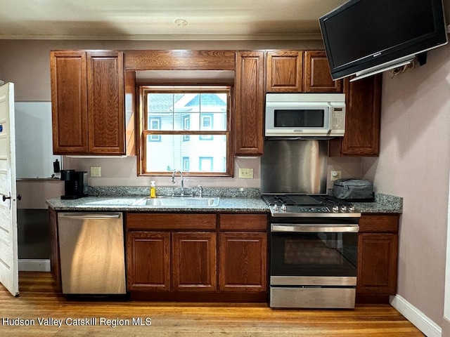 kitchen with appliances with stainless steel finishes, dark stone counters, crown molding, sink, and light hardwood / wood-style floors