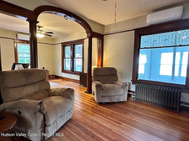 living area featuring radiator, light wood-type flooring, arched walkways, and a wall mounted air conditioner