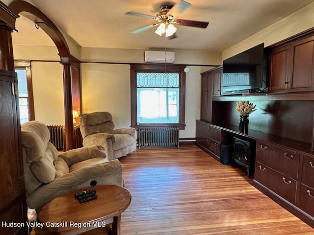 living area with arched walkways, ceiling fan, a wall mounted AC, light wood-type flooring, and radiator