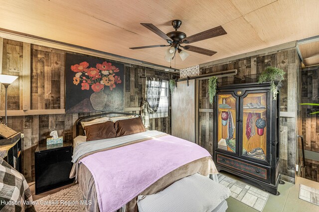 bedroom featuring a barn door, wood ceiling, ceiling fan, and wood walls