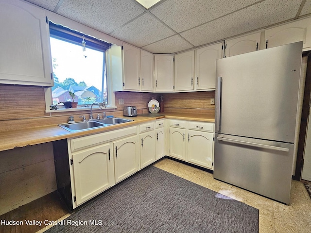 kitchen featuring white cabinetry, stainless steel refrigerator, a paneled ceiling, and sink