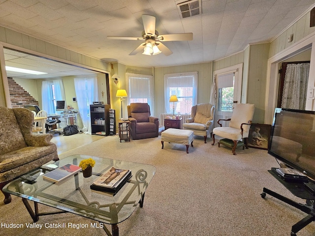 living room featuring carpet floors, ceiling fan, crown molding, and wood walls